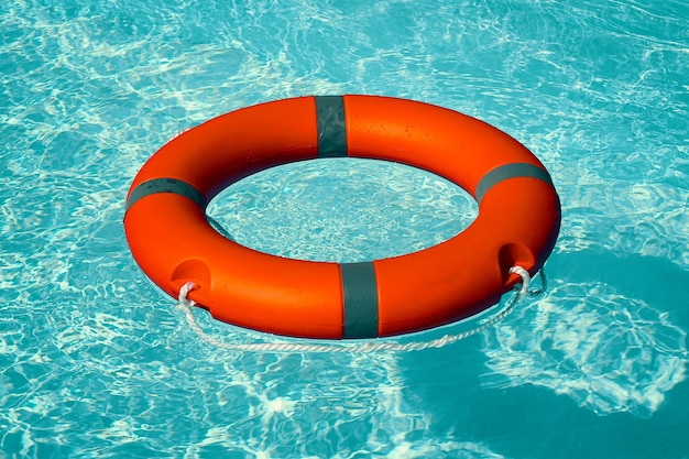 Red lifebuoy pool ring float on blue water.