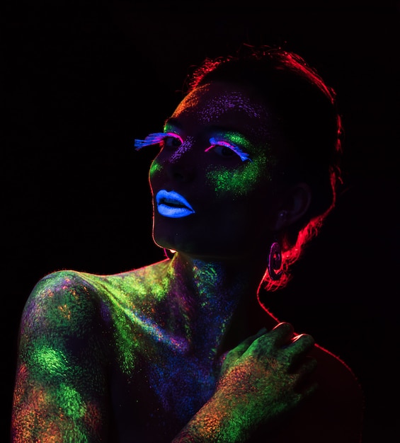 Foto contorno a luce rossa sulla donna sensuale con il trucco di vernice fluorescente