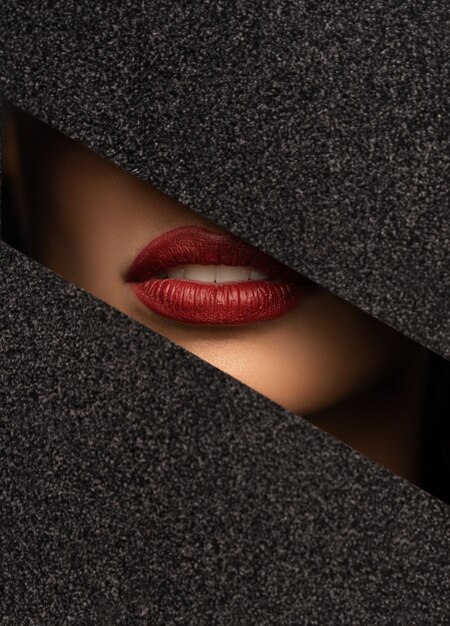 Фото Красные губы заглядывают через отверстие в блестящей черной бумаге