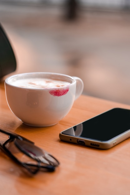 Segno di rossetto rosso su una tazza di caffè sul tavolo al bar