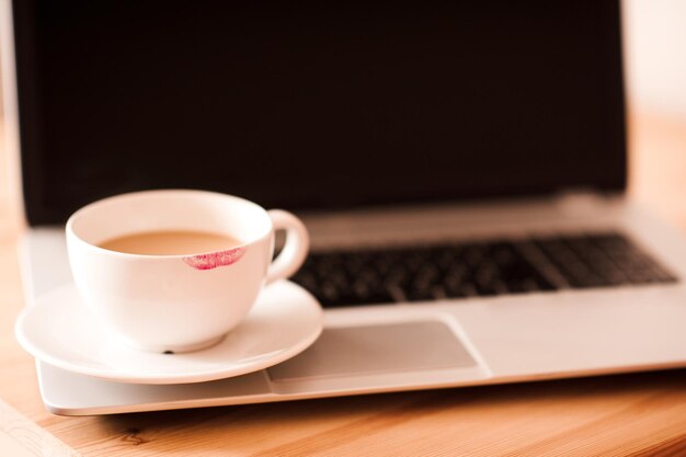 Red lipstick spot on white coffee cup staying on open laptop closeup.