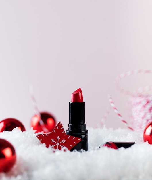 Red lipstick tube and christmas tree baubles on artificial snow pile