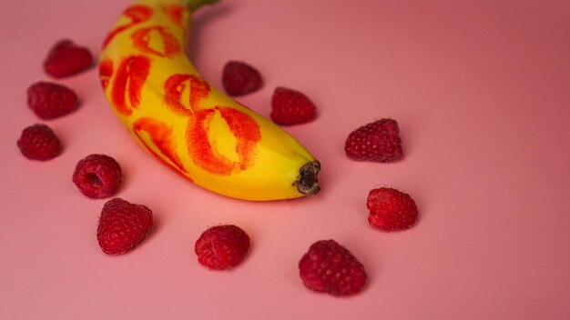 Red lipstick on a yellow banana on a pink background with banana raspberries. Love concept.