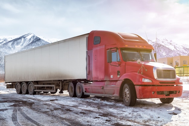 Red long distance truck with a semitrailer at winter on the background of high picturesque mountains