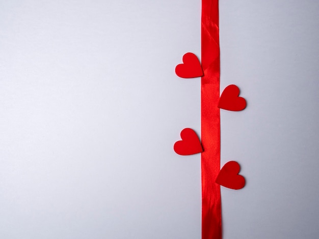 Red long ribbon surrounded by four red hearts on a bright white background