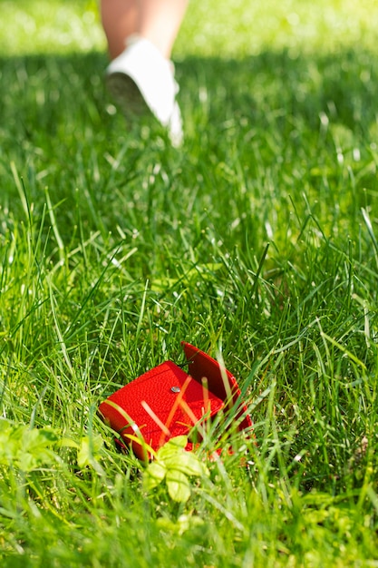 A red lost wallet lies in the grass against the background of a blurred leaving girl Wallet loss