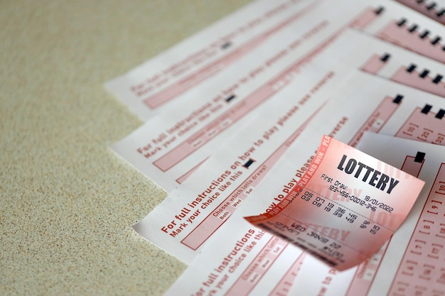 Red lottery ticket lies on pink gambling sheets with numbers for marking to play lottery Lottery playing concept or gambling addiction Close up