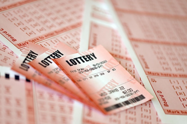 Red lottery ticket lies on pink gambling sheets with numbers for marking to play lottery Lottery playing concept or gambling addiction Close up