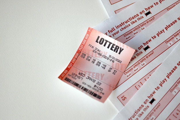 Red lottery ticket lies on pink gambling sheets with numbers for marking to play lottery Lottery playing concept or gambling addiction Close up