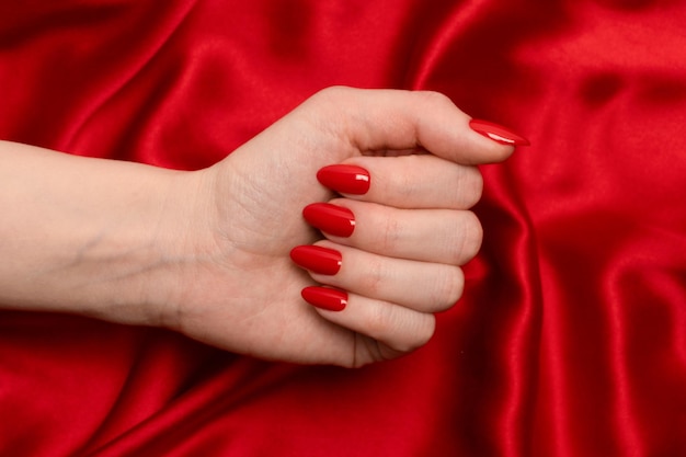 Red manicure on woman hands on a luxury red silk backround