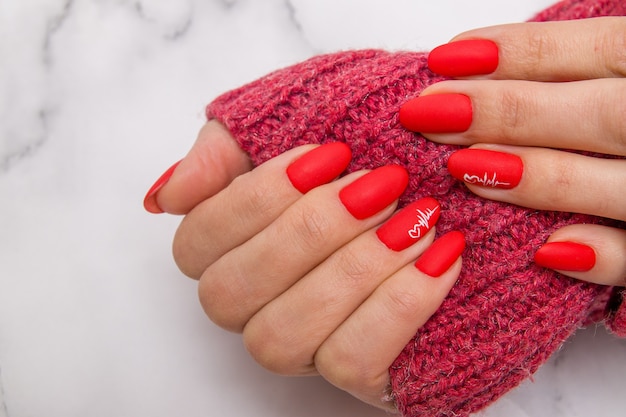 Red matte manicure with a heart pattern and a cardiogram