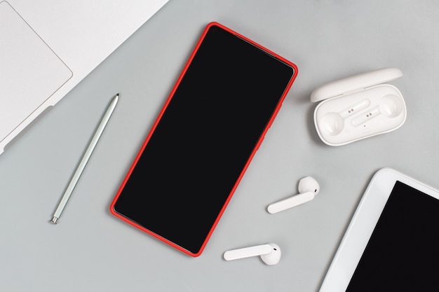 Фото Красный мобильный телефон, наушники и планшет возле ноутбука на белом фоне