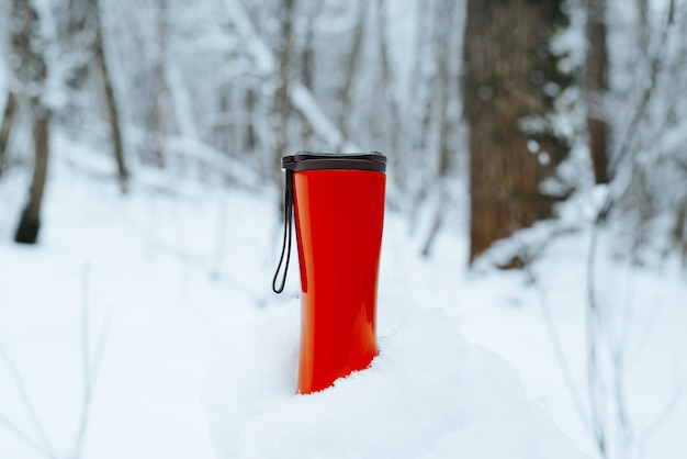 Red modern thermo mug standing in snowdrift in snowy forest on winter day