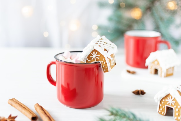 Red mug of hot chocolate with marshmallow and homemade gingerbread small house for decoration