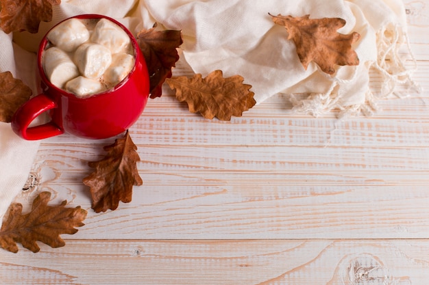 Tazza rossa con cacao e marshmallows, su uno sfondo di una sciarpa e foglie secche. mood autunnale, una bevanda calda.