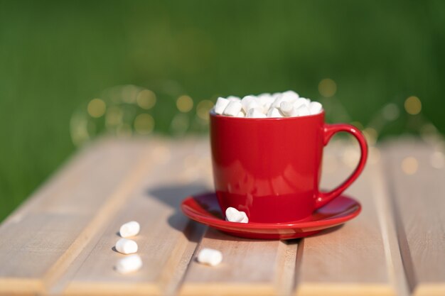 Red mug with cocoa and marshmallows on a wooden table and green background