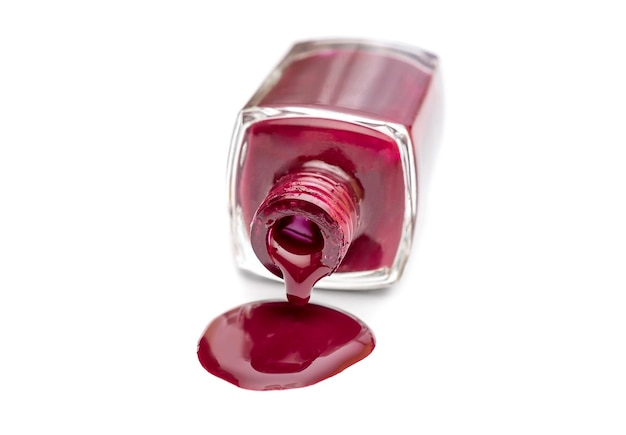 Red nail polish spilled from the bottle on white background