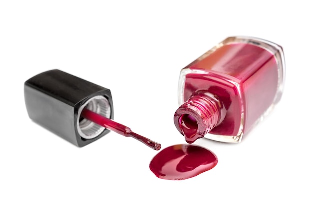 Red nail polish spilled from the bottle with brush on white background