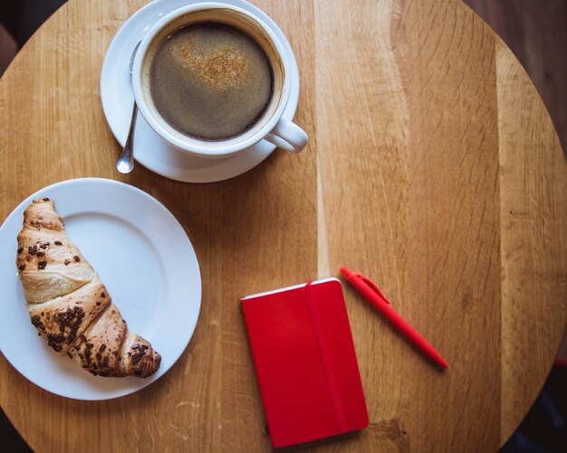 Photo a red note and red pen is on the table in a cafe a cup of coffee and a croissant