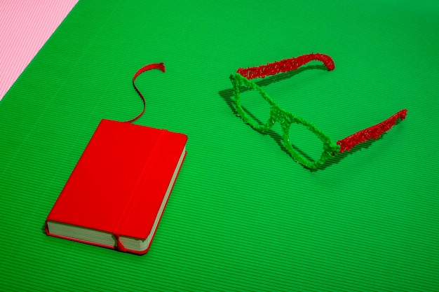 Red notebook with colored glasses on a green background