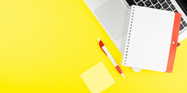 Red notepad, pen, colorful clips and laptop on yellow