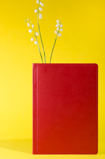 Red notepad with lily of the valley flowers on a yellow background