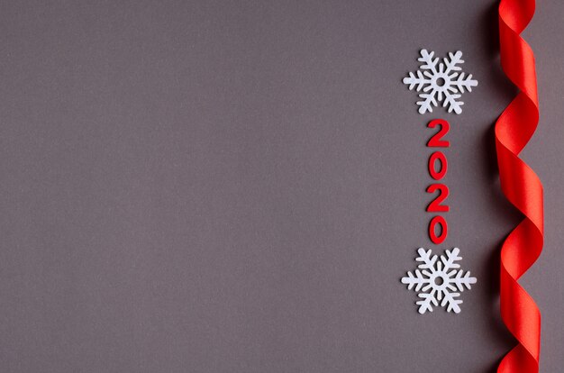 Red number 2020, ribbon and white snowflakes composition on dark background, New Year and Christmas holiday.