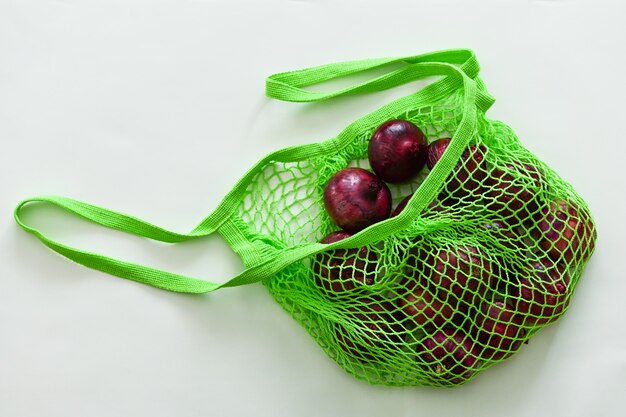 Red onion in a green string bag on a grey surface