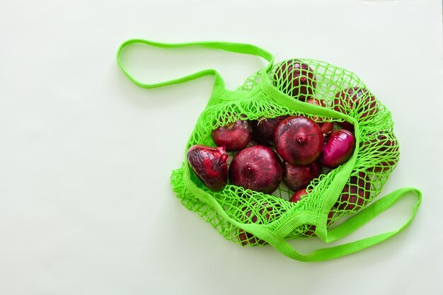 Red onion in a green string bag on a wooden table