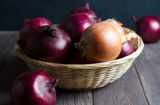 Red onions in a wicker basket. Brown wooden table.