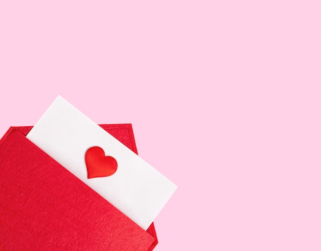 Красный открытый конверт с листом бумаги с сердцем на розовом фоне с copyspace. День святого Валентина