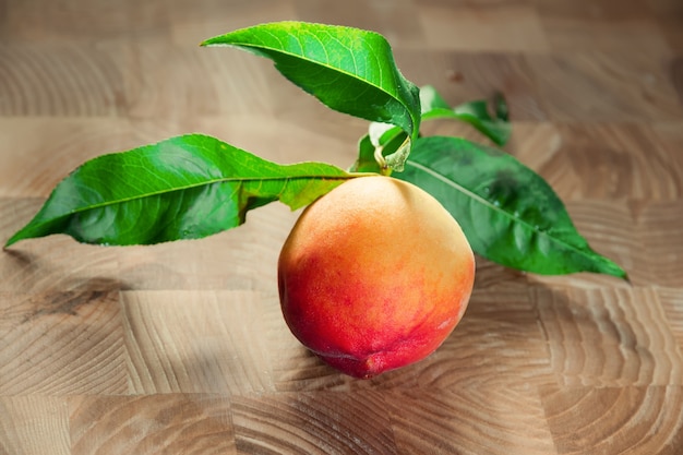 A red-orange ripe peach with leaves on the wooden board