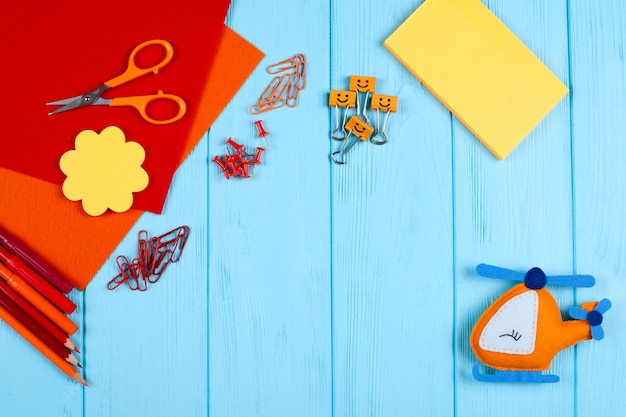 Red and orange stationery and felt helicopter on blue wooden background.