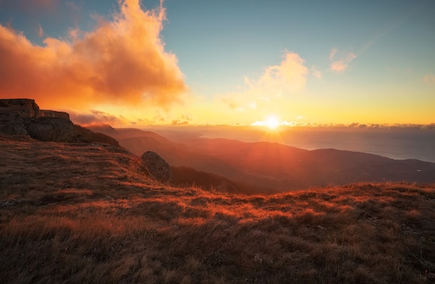 秋の山の赤とオレンジ色の夕日。日当たりの良い梁のある風景