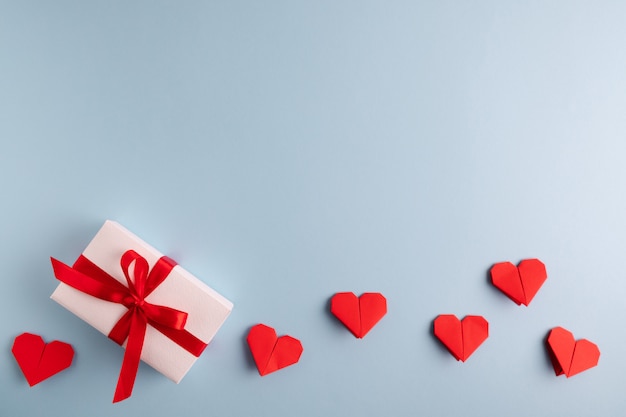red origami hearts and present on a pastel blue table.