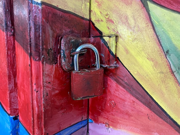 A red padlock is on a wall with a colorful background.