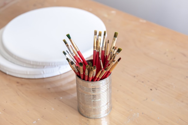 Premium Photo  Red paint brushes in a metal can on a table with round  canvases for painting.