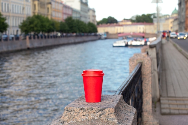 Red paper cup of coffee on railing on river embankment