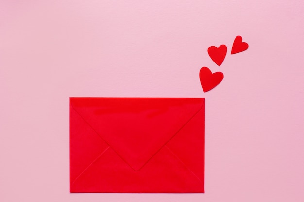 Red paper envelope and small red hearts lying on a pink background