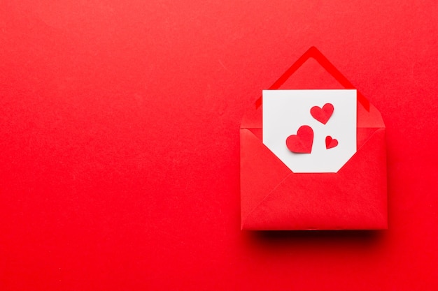 Red paper envelope with empty white card and heart on colored background top view valentines day concept