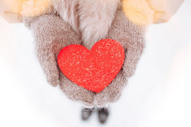 Red paper hearts in the hands of a woman wearing woolen mittens outside at a snowy winter park. Romantic woman celebrates Valentine's day with symbols of love. Sign of 14 February.