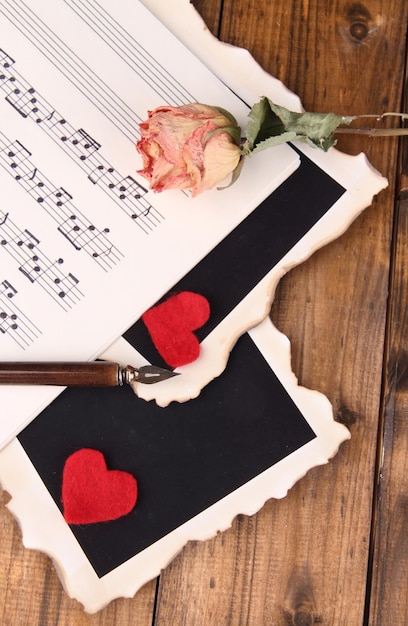 Photo red paper hearts photos on music book closeup on wooden background