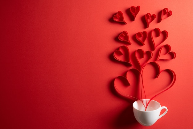 Red paper hearts splash out from coffee cup