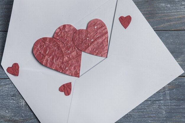 Red paper hearts with envelope on wooden surface