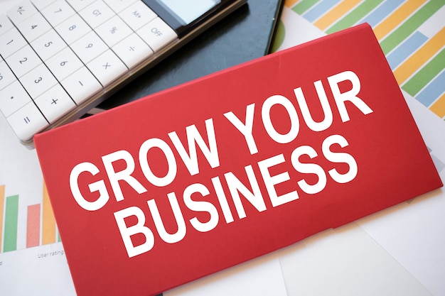 Photo red paper sheet with the text grow your business, calculator and pen on the desktop. business concept