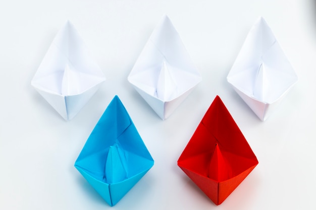 Красный бумажный кораблик и синий бумажный кораблик, ведущий среди кораблей белой бумаги