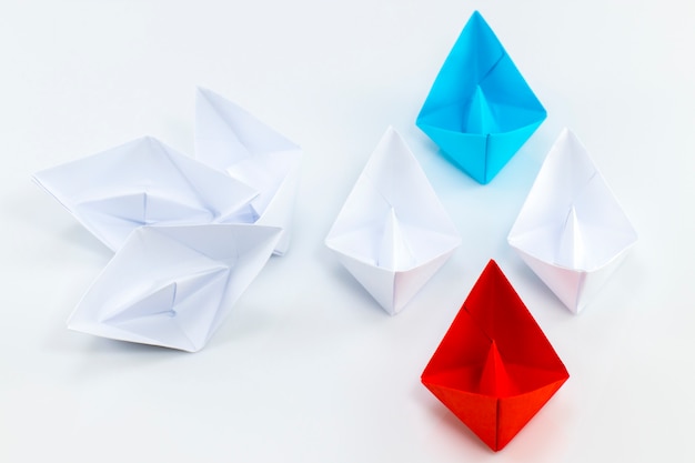 Red paper ship and blue paper ship leading among white paper ships