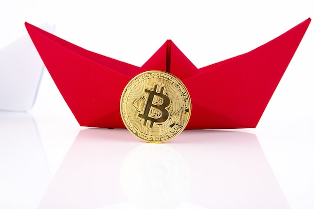 Red paper ship, golden bitcoin isolated on white