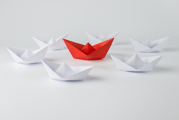 Red paper ship leading among white background