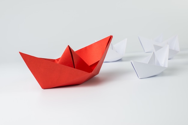 Red paper ship leading among white